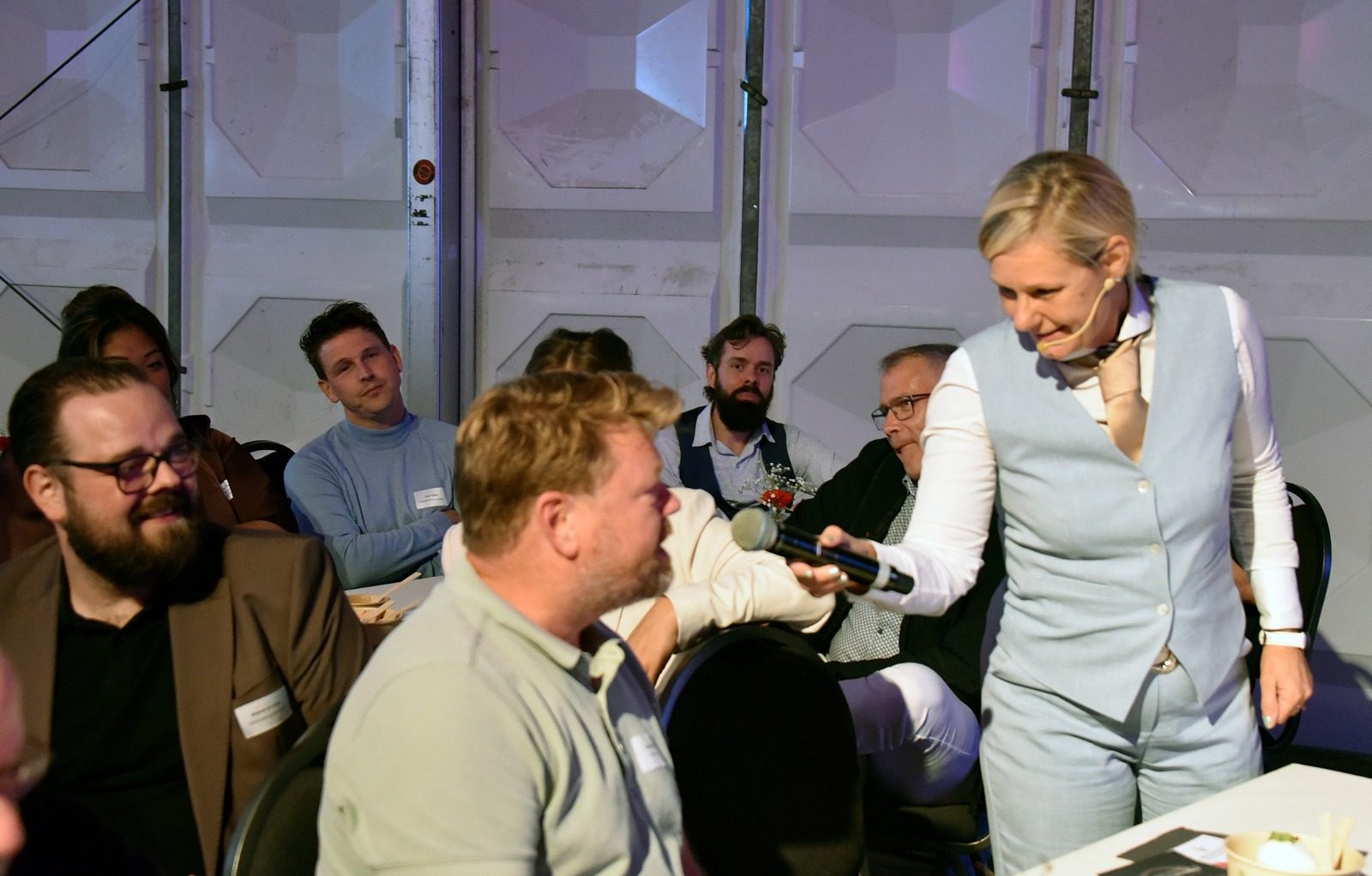 De presentatrice houdt een microfoon voor een bezoeker in de zaal