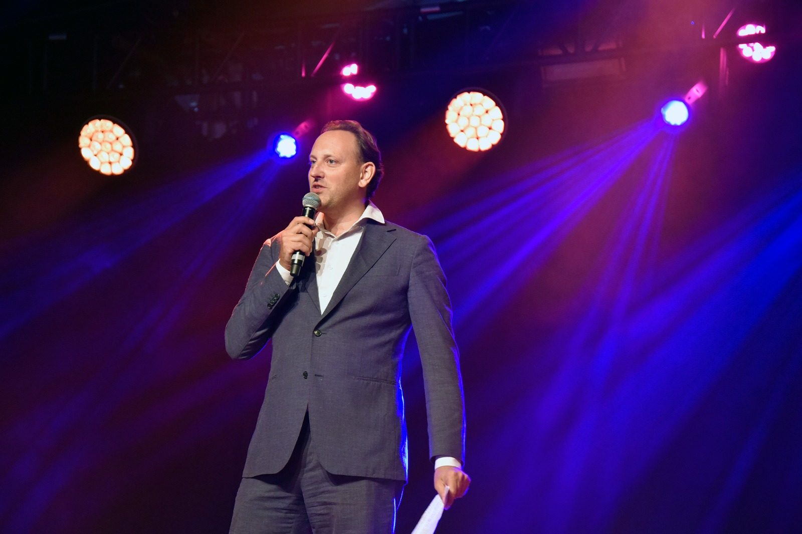 Een spreker met microfoon en papieren in de hand op het podium